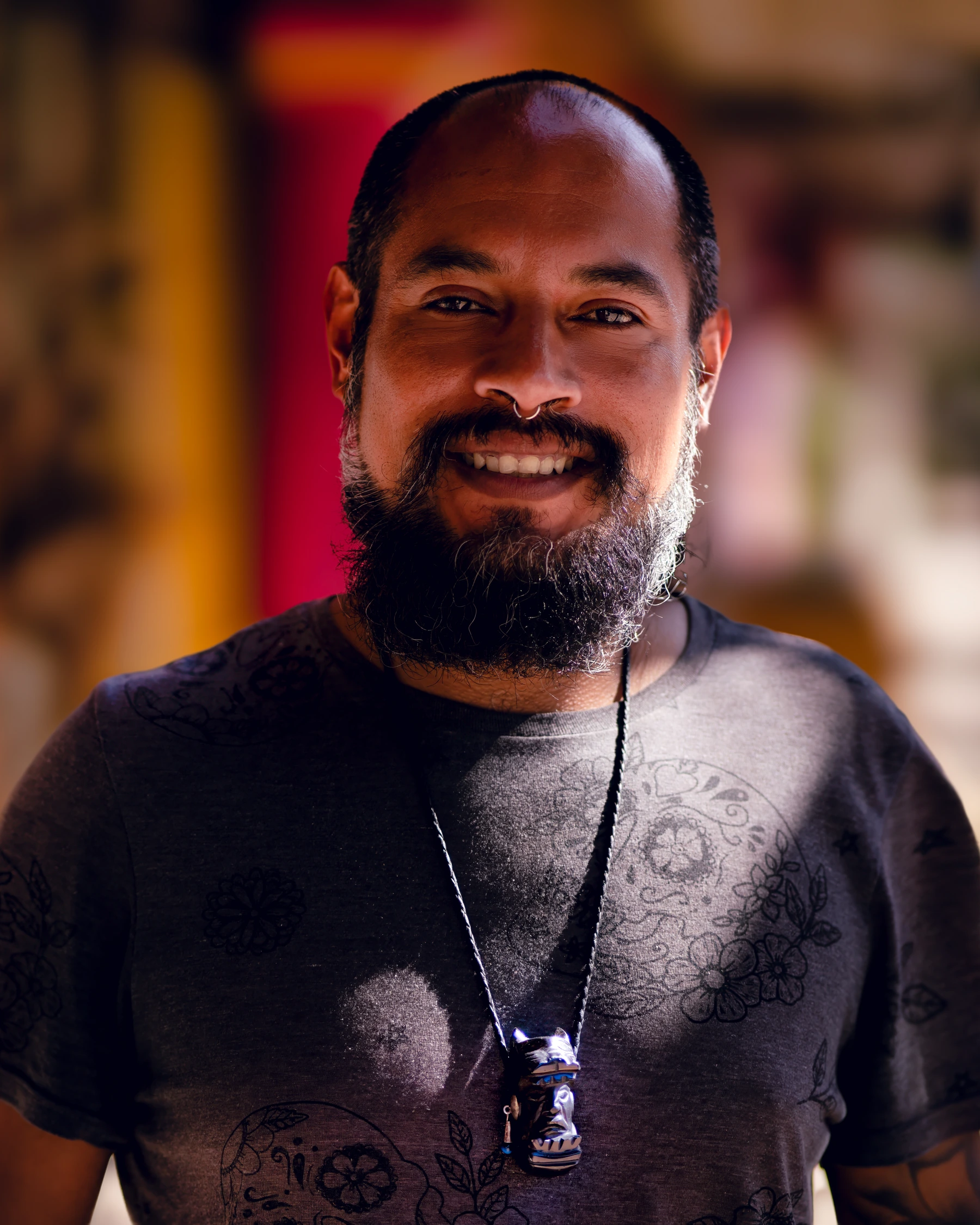 Portrait of a smiling man with a beard, septum ring and carved pendant.
