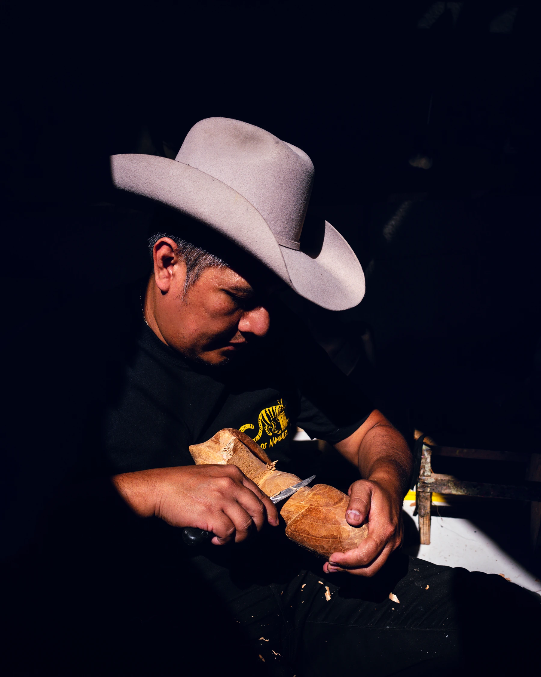 Roque Jimenez wearing a light cowboy hat and carefully carving a wooden form with a hand tool.